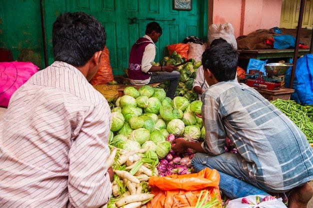 A close-up photo of a bustling Bangladeshi marketplace with vendors selling various goods and fresh produce. The image is filled with vibrant colors and textures, illustrating the daily commerce activities and potential supply chain issues contributing to inflation. The focus is sharp, capturing the economic activity.