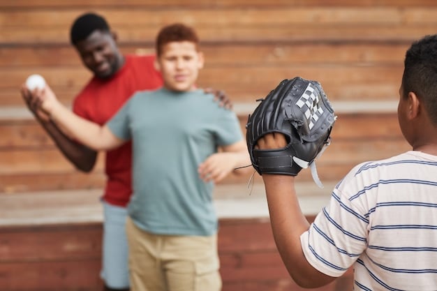 A cricket coach demonstrating a spin bowling grip to a group of young cricketers on a sunny cricket field. The coach is holding a cricket ball and pointing out the finger placement.