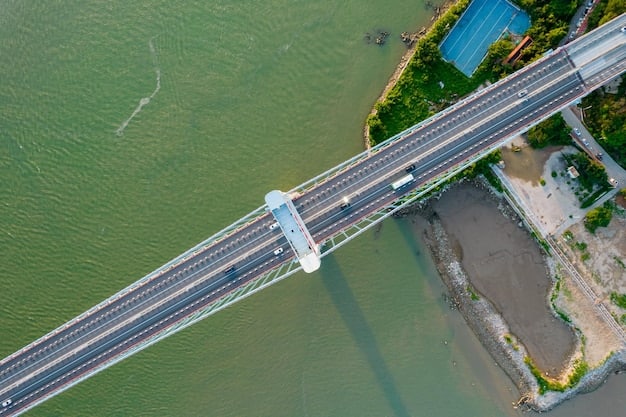An aerial view of the Padma Bridge, showing the six lanes of traffic and the railway track in the middle. The river is wide and flowing, and there are green fields on either side.