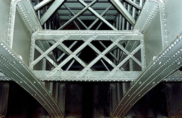 A close-up of one of the Padma Bridge's pillars, showing the intricate steel and concrete construction. Workers are visible on the bridge, and the river flows below.