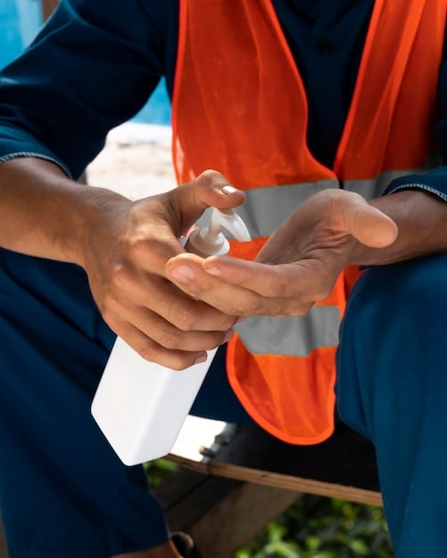 A photo showing a community health worker inspecting a water container for mosquito larvae. The setting is a residential area with houses in the background. The health worker is using a flashlight and magnifying glass to check for larvae in standing water inside the container.