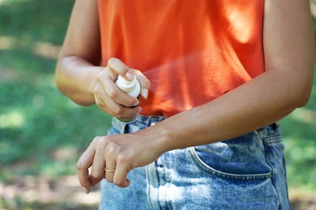 A photograph showing a woman applying mosquito repellent on her arms and legs. She is indoors, and the background is a typical home setting. The focus is on her applying the repellent spray.